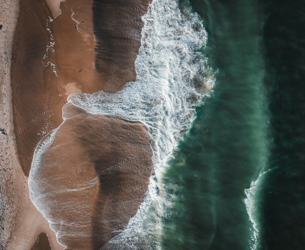 Waves washing onto a sandy shoreline from above