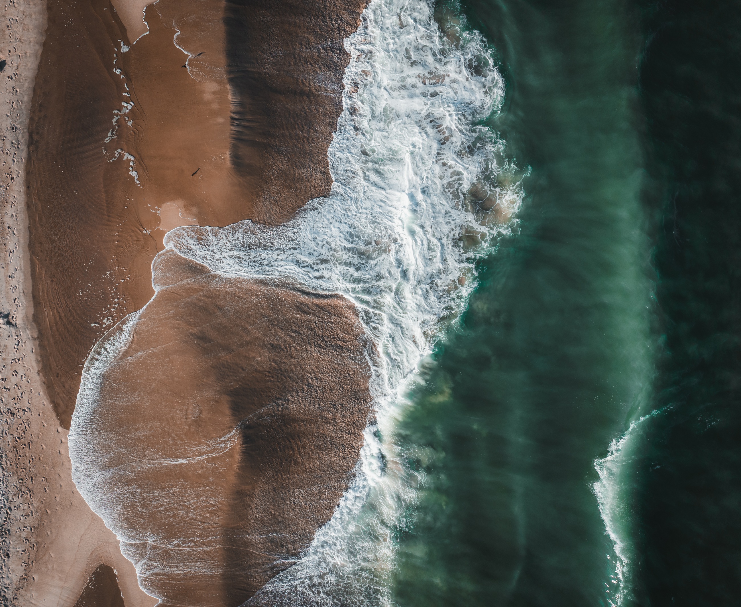 Waves washing onto a sandy shoreline from above