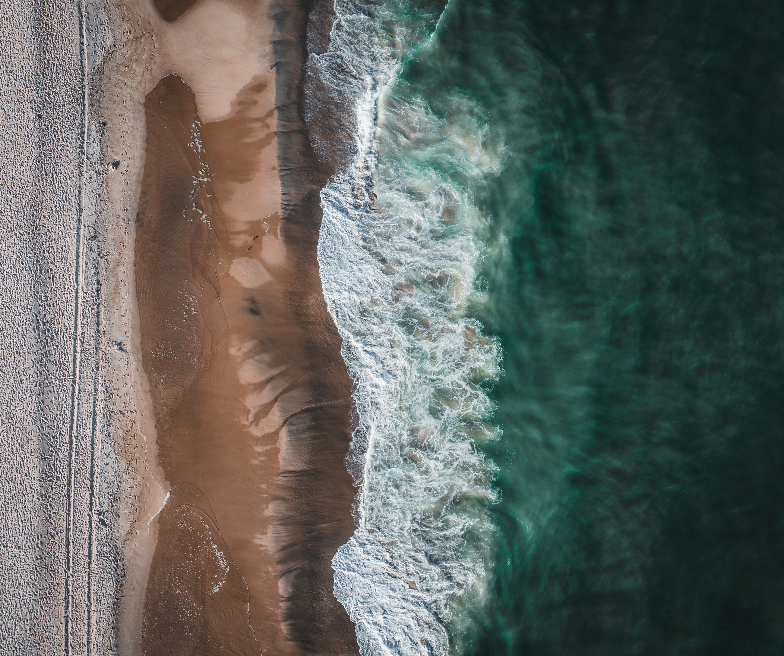 Turquoise surf along a sandy beach from above